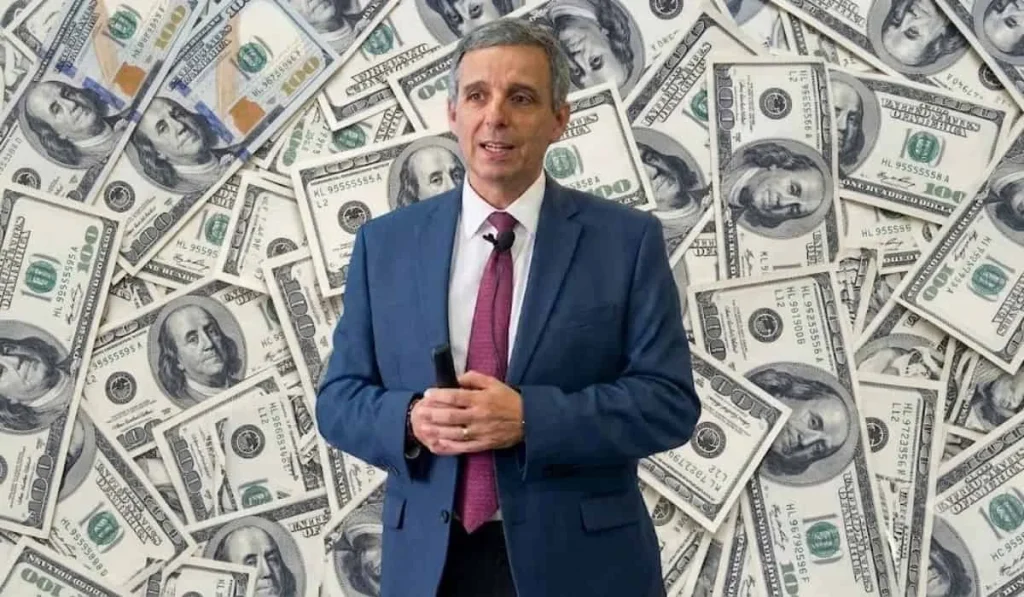 Montaje de un funcionario de Hacienda sobre un fondo de billetes de dólares. Referencia a recorte al presupuesto de 2026